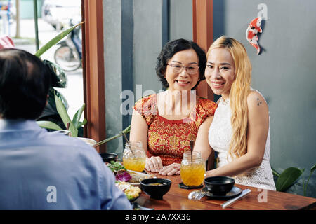 Felice piuttosto giovane donna vietnamita in posa con la sua madre quando si è seduti al ristorante tabella Foto Stock