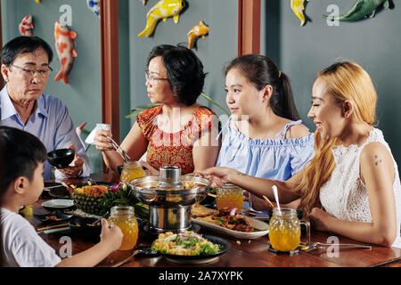 Felice famiglia vietnamita di mangiare piatti tradizionali e a discutere di novità al tavolo per la cena in cafe Foto Stock