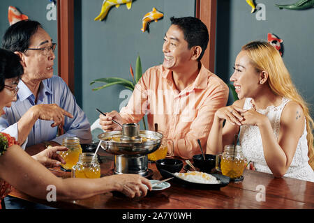 Allegro Coppia matura e i loro genitori senior parlando e scherzando quando a cena a casa insieme Foto Stock