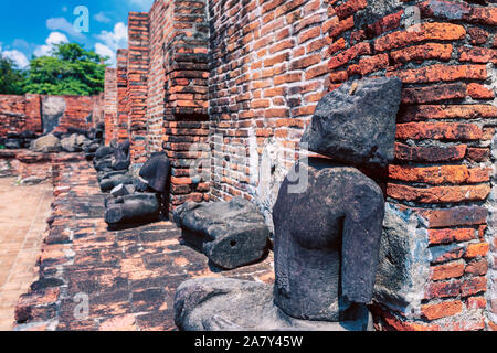 Statue di roccia siedono lungo una parete di frantumazione a metà giornata con i cieli blu intorno alla antica città di Ayutthaya, a nord di Bangkok, Thailandia Foto Stock