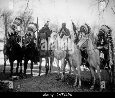 Sei capi tribali (l a r) Poco Plume (Piegan), Charley Daino (UTE), Geronimo (Apache Chiricahua), Quanah Parker (Comanche), Cavo avvisatore acustico Bear (Brulé Sioux), e Cavallo americano (Oglala Sioux) a cavallo in vesti cerimoniali Foto Stock