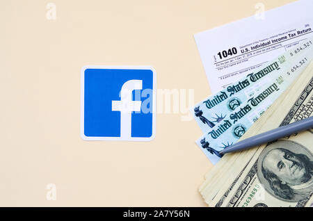 KHARKOV, Ucraina - 3 ottobre 2019: Facebook logo stampato si trova con 1040 singoli redditi modulo con assegno di rimborso e centinaia di fatture del dollaro Foto Stock