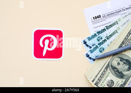 KHARKOV, Ucraina - 3 ottobre 2019: Pinterest logo stampato si trova con 1040 singoli redditi modulo con assegno di rimborso e centinaia di fatture del dollaro Foto Stock