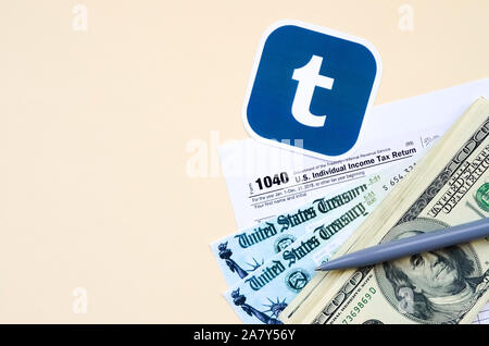 KHARKOV, Ucraina - 3 ottobre 2019: Tumblr logo stampato si trova con 1040 singoli redditi modulo con assegno di rimborso e centinaia di fatture del dollaro sul Foto Stock