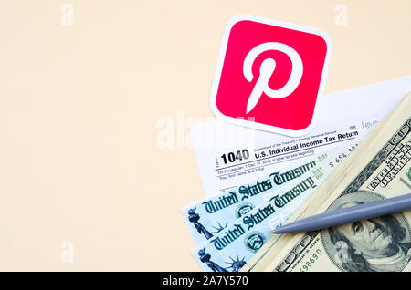 KHARKOV, Ucraina - 3 ottobre 2019: Pinterest logo stampato si trova con 1040 singoli redditi modulo con assegno di rimborso e centinaia di fatture del dollaro Foto Stock