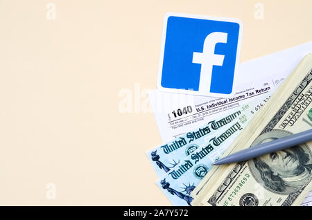 KHARKOV, Ucraina - 3 ottobre 2019: Facebook logo stampato si trova con 1040 singoli redditi modulo con assegno di rimborso e centinaia di fatture del dollaro Foto Stock