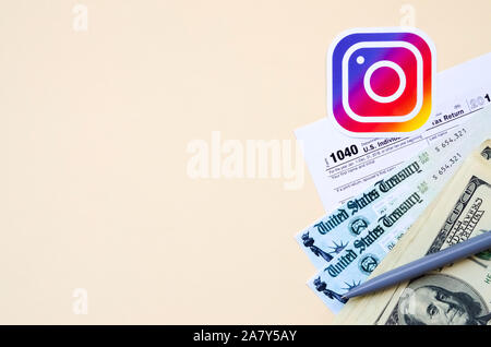 KHARKOV, Ucraina - 3 ottobre 2019: Instagram logo stampato si trova con 1040 singoli redditi modulo con assegno di rimborso e centinaia di fatture del dollaro Foto Stock