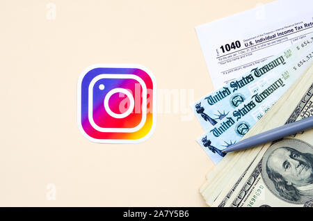 KHARKOV, Ucraina - 3 ottobre 2019: Instagram logo stampato si trova con 1040 singoli redditi modulo con assegno di rimborso e centinaia di fatture del dollaro Foto Stock