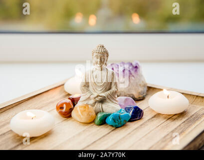 Tutti i sette colori dei chakra pietre cristalli attorno seduti BUDDA STATUETTA IN LEGNO NATURALE vassoio. Equilibrio e calma il flusso di energia nel concetto di casa. Foto Stock