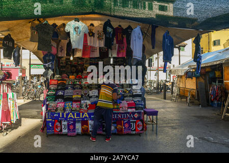 Una politica estera venditore ambulante disponendo le merci sul suo stallo di souvenir t-shirt in San Lorenzo Piazza del Mercato Centrale, Firenze, Toscana, Italia Foto Stock