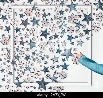 Vacanze invernali concetto. La mano della donna in maglia maglione rendere stelle blu e fiocchi decorativi composizione pattern nel telaio su sfondo bianco. La Cre Foto Stock