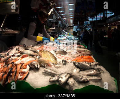 Barcellona, Spagna - 3 Maggio 2017: al Mercado de La Boqueria / mercato La Boqueria. Un pescivendolo posa un ben fornito mercato pesce stallo a una via Foto Stock
