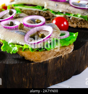 Panino con le aringhe salate, il burro e la cipolla rossa sul vecchio rustico tagliere. Messa a fuoco selettiva Foto Stock