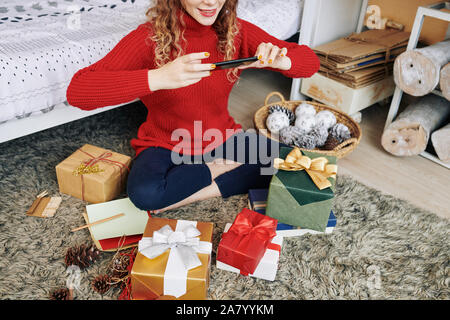 Immagine ritagliata positivo della giovane donna fotografare avvolto nuovo anno presenta per i suoi amici Foto Stock