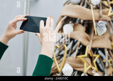 Le mani della giovane donna utilizza lo smartphone quando si scattano foto di tree ha decorato per il Natale Foto Stock