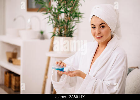 Bella donna in accappatoio e asciugamano utilizza tonico o una lozione prodotto. ragazza con detergenti per la pelle. Foto Stock
