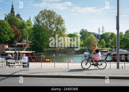 Donna ciclismo, vista in estate di una giovane donna in bici Strandvägen, un lungomare ciclabile su Östermalm nel centro di Stoccolma, in Svezia. Foto Stock