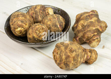 Gruppo di sei intere fresche brown carciofo di Gerusalemme in ceramica scura ciotola di legno bianco Foto Stock