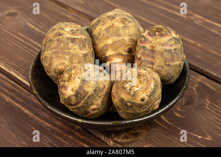 Il gruppo di cinque intere fresche brown carciofo di Gerusalemme in ceramica scura ciotola di legno marrone Foto Stock