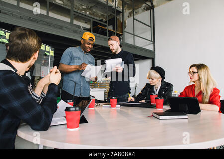 Gruppo giovane gente di affari riuniti a discutere di idea creativa. Gruppo di studenti internazionali seduta a tavola con caffè e computer e Foto Stock