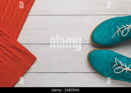 Il turchese donne scarpe con lacci e arancione brillante felpa lavorata a maglia sulla luce sullo sfondo di legno. Il concetto di moda, vista dall'alto. Uno stile di vita informale in autunno. Fla Foto Stock