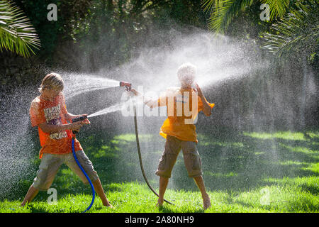 Fratelli giocando con giardino hosepipes Foto Stock