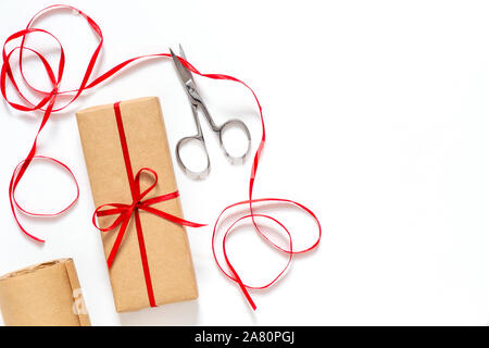 Confezione regalo di imballaggio. Forbici, nastro rosso, carta kraft su uno sfondo bianco. Orientamento orizzontale, copia dello spazio. Foto Stock