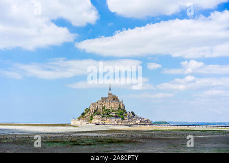 Vista in lontananza Mont Saint Michel durante la bassa marea ovest della Francia con le nuvole nel cielo blu Foto Stock