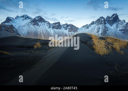 Snowy Vestrahorn montagna, in Stokknes, sud-est dell'Islanda. Dopo il tramonto. Le dune di sabbia, erba e il mare. Foto Stock