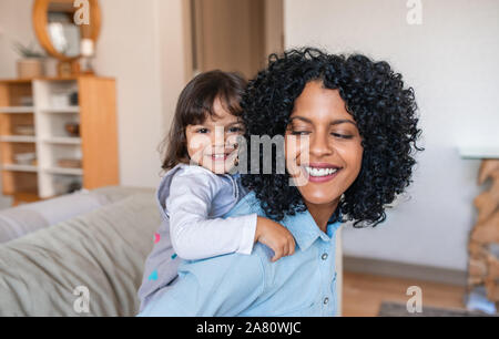 Sorridente mom piggybacking la sua adorabile figlia intorno alla casa Foto Stock