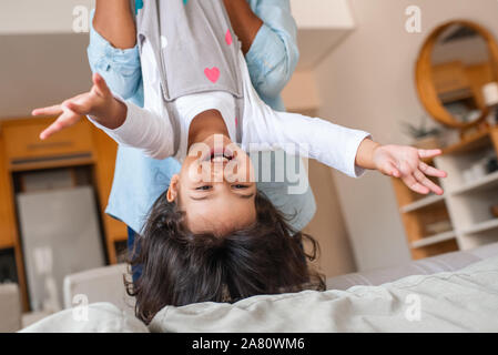 Ridere piccola figlia essendo tenuta capovolta da sua mamma Foto Stock