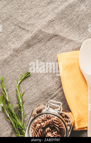 Materie in grani interi di pasta italiana su un telo di lino in cucina - rosmarino e fusilli - vista superiore dello spazio di copia Foto Stock