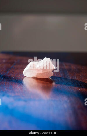 La guarigione è salito in cristallo o una gemma su di un tavolo di legno. Una graziosa rosa pietra amore isolate portare buone vibes e vibrazioni positive Foto Stock