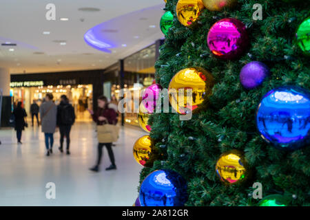 Christmas Shopper camminare davanti a un albero di Natale decorato con luminosi baubles in un centro commerciale per lo shopping Foto Stock
