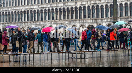 I turisti in una piovosa Venezia utilizzando duckboards di passeggiare in un invaso Piazza San Marco ad alta marea Foto Stock