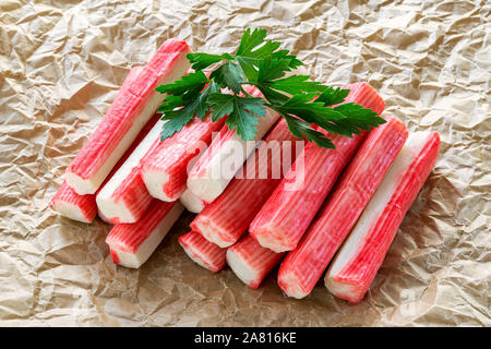 Cumulo di surimi bastoncini di granchio con il prezzemolo una accartocciata carta pergamena. Piatti a base di frutti di mare e come ingrediente per insalate. Mangiare sano e cuocere a casa. Vista frontale. Foto Stock