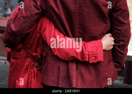 Giovane indossando matching cappotti rossi abbracciare ogni altro- vista posteriore, London, Regno Unito Foto Stock