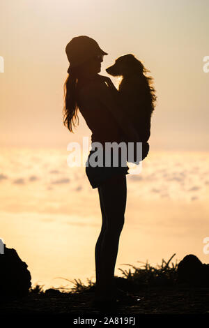 Silhouette di una ragazza con cucciolo sul tramonto Foto Stock