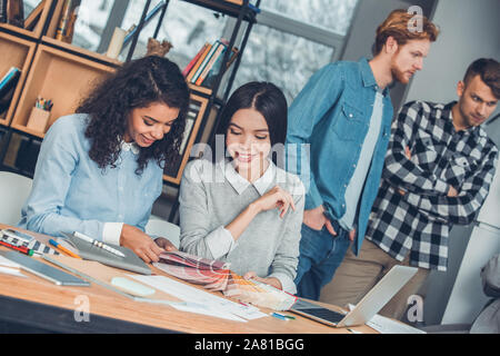 Startupers lavorando insieme a Office designer femmina seduta a tavola scegliendo il colore dalla tavolozza felice Foto Stock