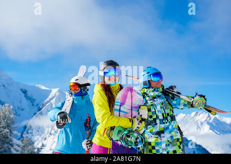 Due uomini e una donna con lo snowboard e sci cercando in direzioni diverse in piedi sulla neve località sullo sfondo di montagne e di cielo nuvoloso dopo Foto Stock