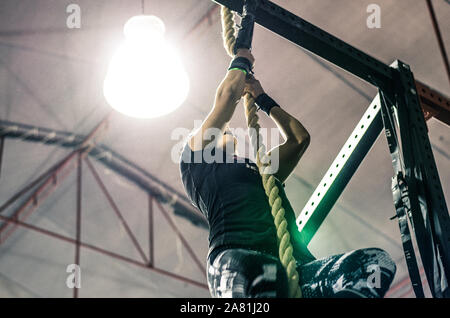 Irriconoscibile atletica giovane donna che lavorano e arrampicata corda in una palestra Foto Stock