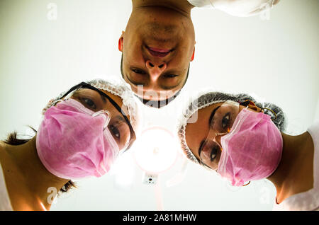 Ritratto di tre chirurghi al lavoro, operanti in uniforme, guardando la telecamera Foto Stock