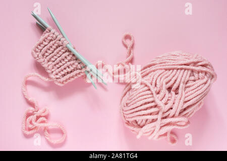 Sfera della filettatura e aghi da maglia su sfondo rosa, avviare i guanti a maglia Foto Stock
