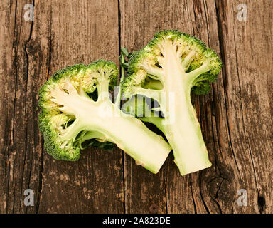 Broccoli, uno tagliato a metà, appoggiata su un vecchio tavolo, Foto Stock