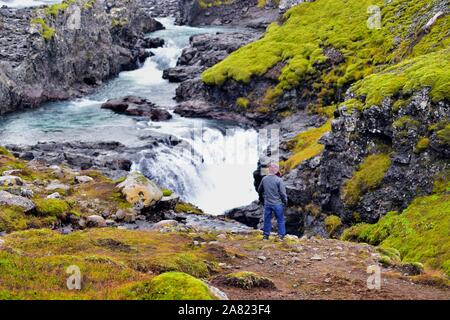 Distretto Hróarstunga, Islanda. Turisti ed escursionisti guardando il flusso della cascata Sveinstekksfoss come correnti verso il mare in Oriente Islanda. Foto Stock