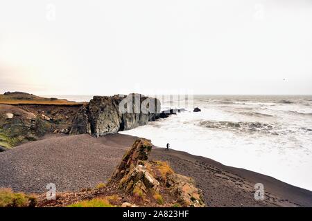 Oriente fiordi, Islanda.Lone visite turistiche di una spiaggia di sabbia nera di saltare le rocce nel surf. L'area delle spiagge formate da attività vulcanica sono spruzzati in Foto Stock