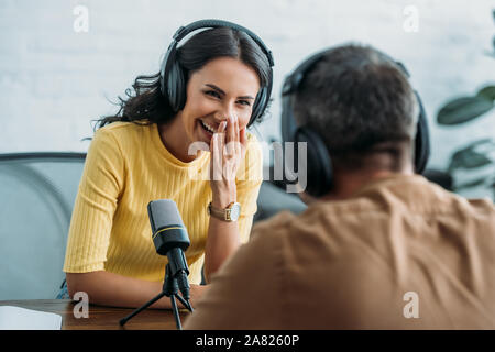 Messa a fuoco selettiva di allegro host radio ridendo durante la registrazione di podcast con un collega Foto Stock