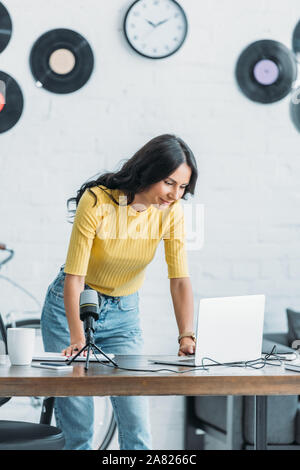 Radio interessante host utilizzando computer portatile mentre si sta in piedi in workplace in studio Foto Stock