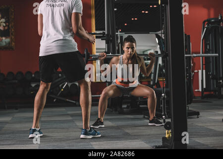 Vista ritagliata della personal trainer guardando i giovani sportive il sollevamento barbell Foto Stock