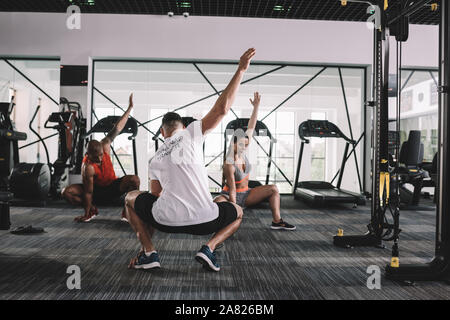 Vista posteriore del trainer squatting con mano sollevata insieme con gli atleti multiculturale Foto Stock